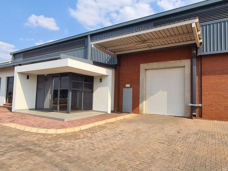 Modern industrial unit featuring a brick and metal facade, a large roller shutter door, and a dedicated glass-fronted entrance with paved driveway access.
