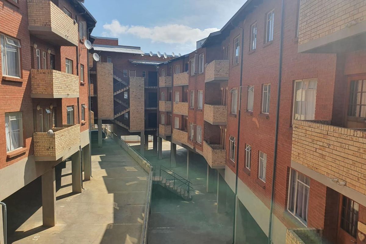 Exterior view of an apartment complex featuring face brick facades, multiple balconies, and a central paved courtyard area with structural concrete supports.
