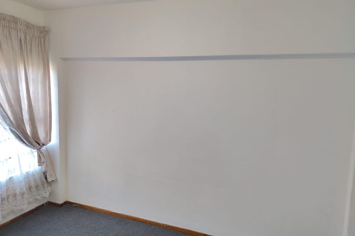 A simple, neutral bedroom space featuring carpeted flooring and a large blank wall, offering a clean canvas for personalization.