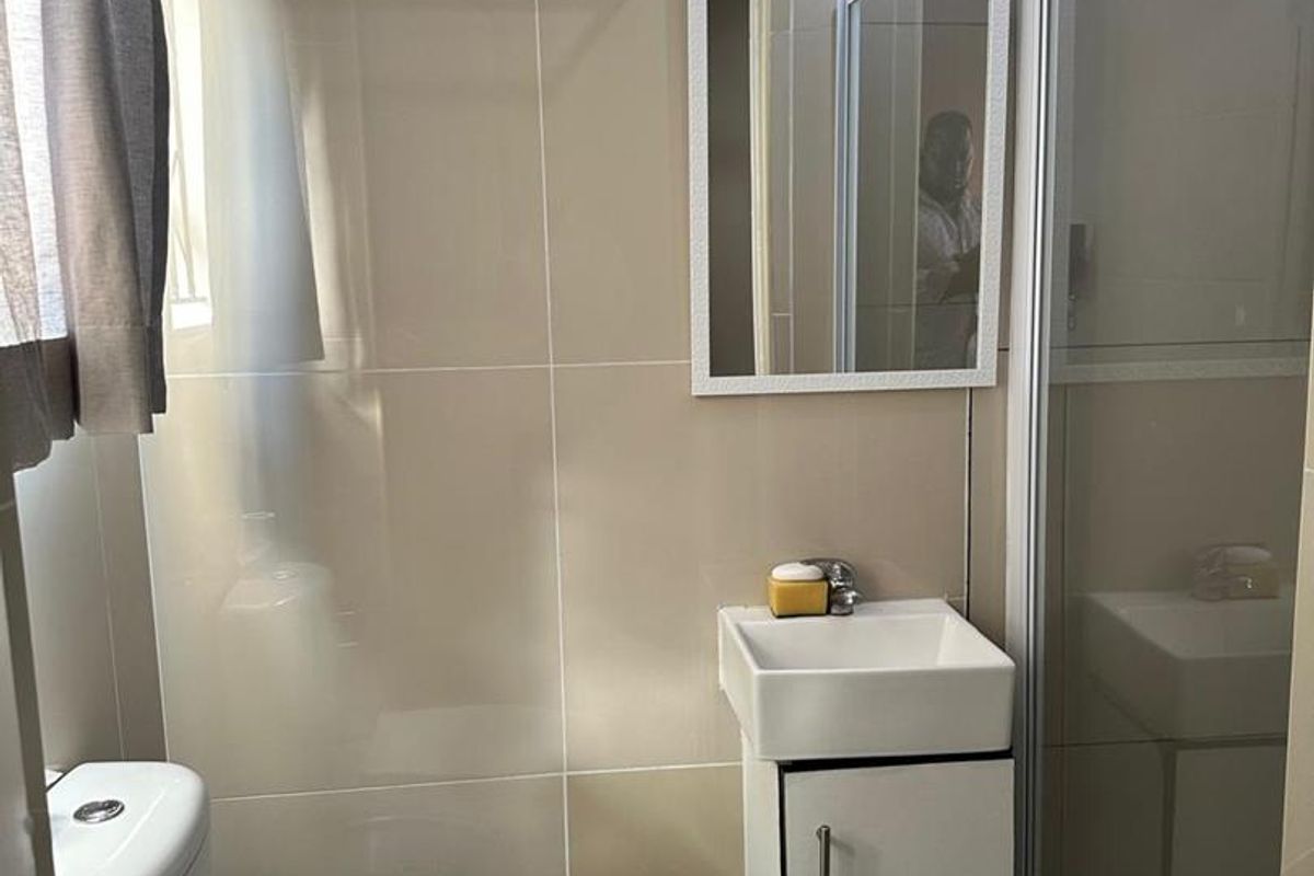 A compact bathroom featuring a shower enclosure, vanity basin, toilet, and neutral wall tiling.