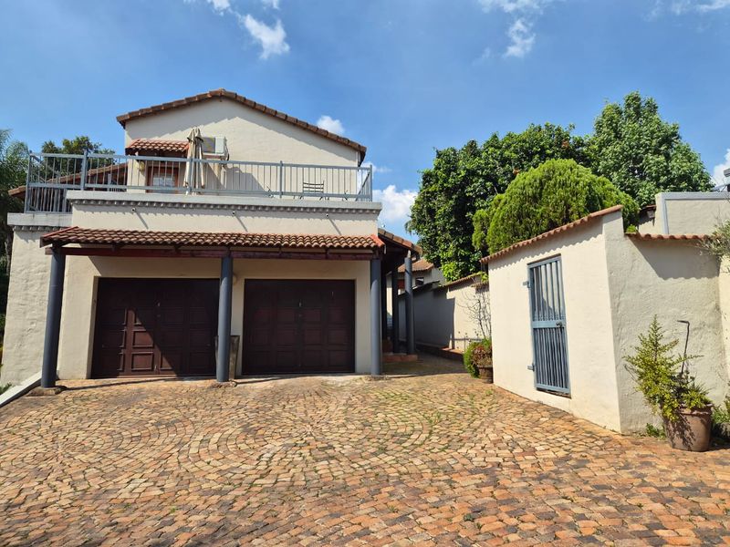 Front exterior view featuring a double garage, paved cobblestone driveway, and an upper-level balcony with metal railings.