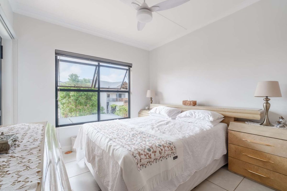 A bright bedroom featuring tiled flooring, a ceiling fan, and a large window providing natural light and an exterior view.