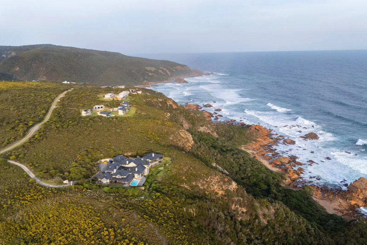 An aerial view of a coastal residential property situated on a cliffside, showcasing the surrounding natural landscape and ocean coastline.