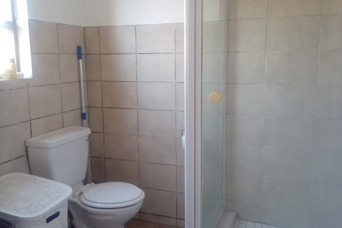 A functional bathroom featuring a shower enclosure, ceramic wall and floor tiling, and a standard toilet.