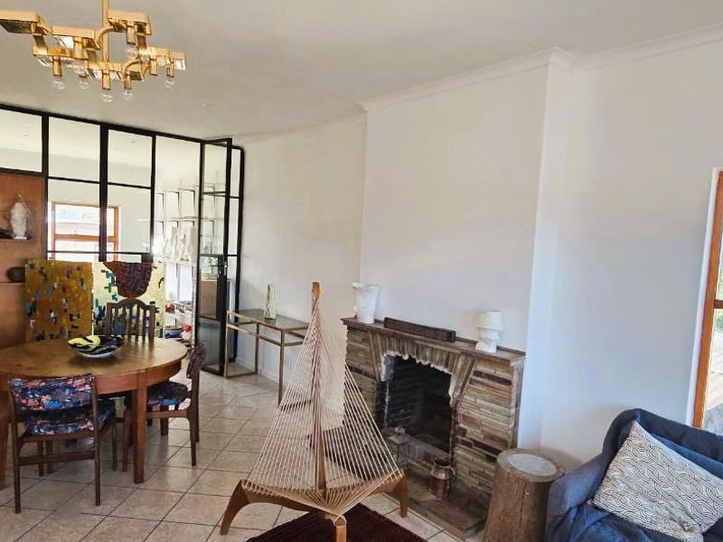 Open-plan living and dining area featuring a stone fireplace, tiled flooring, and a distinctive metal-framed glass partition.