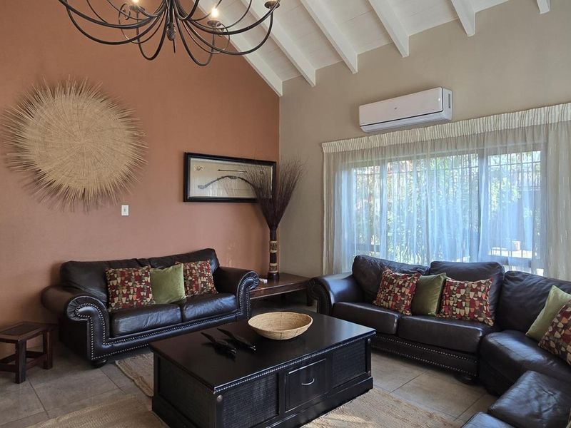 Spacious living room featuring high vaulted ceilings with exposed rafters, tiled flooring, and a wall-mounted split-system air conditioner.
