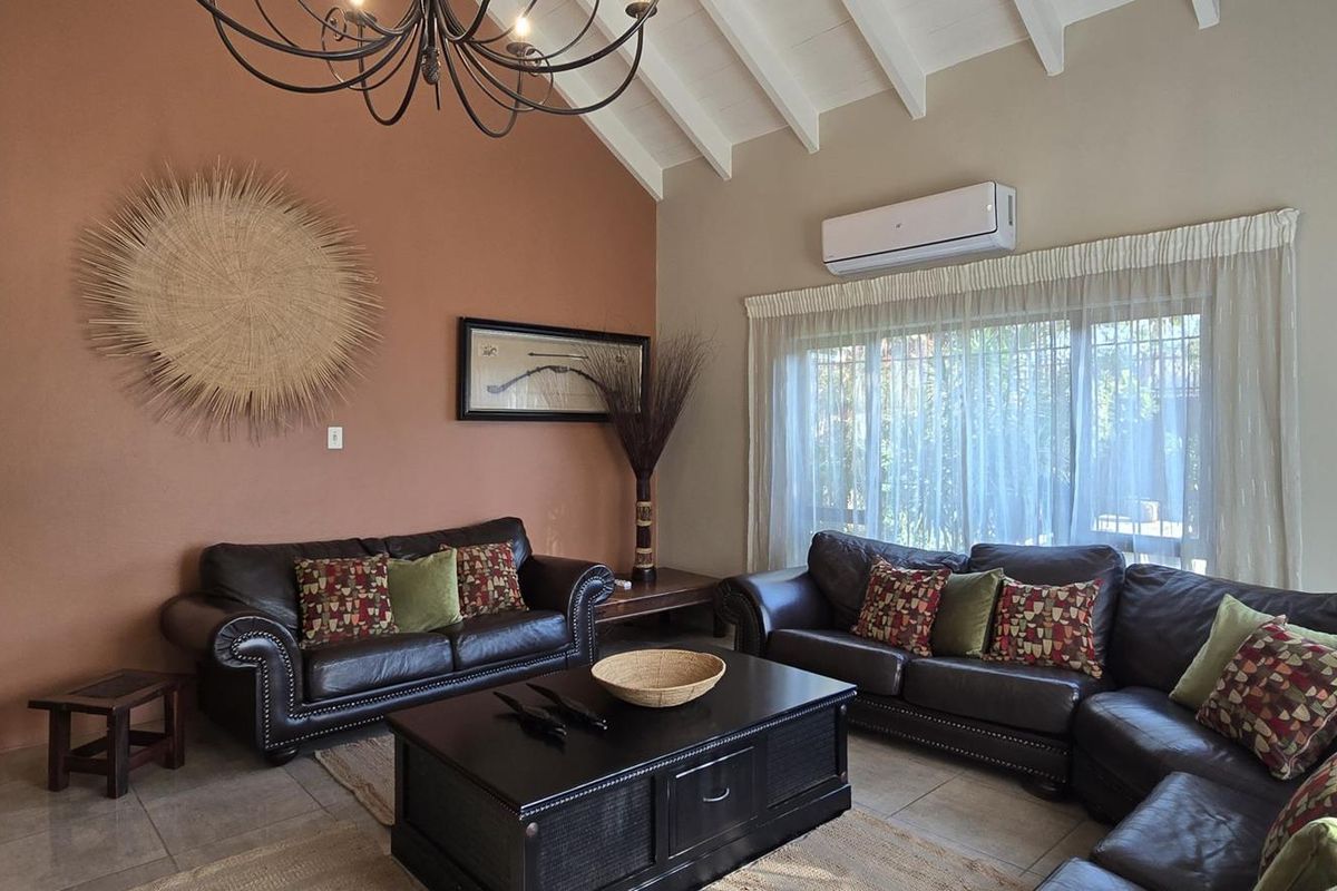 Spacious living room featuring high vaulted ceilings with exposed rafters, tiled flooring, and a wall-mounted split-system air conditioner.