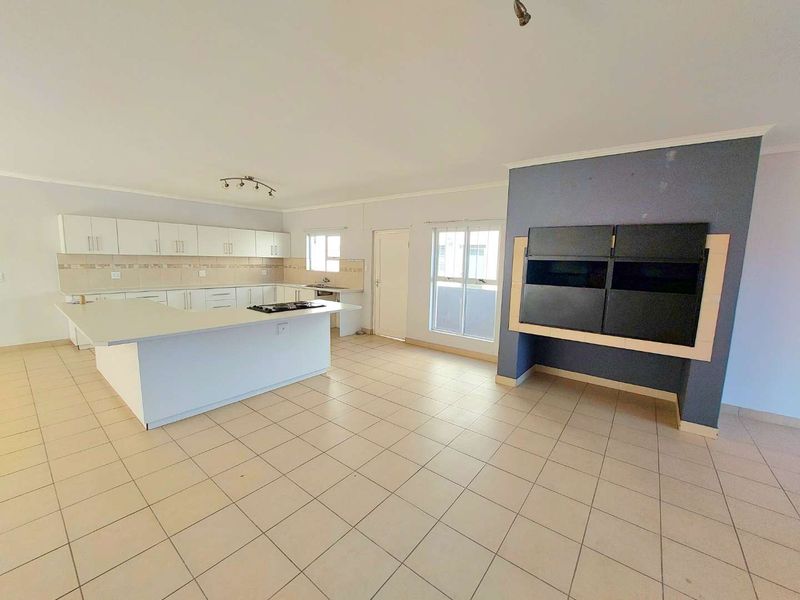 Spacious open-plan living and kitchen area featuring tiled flooring, a central kitchen island with a gas hob, and a prominent built-in fireplace.