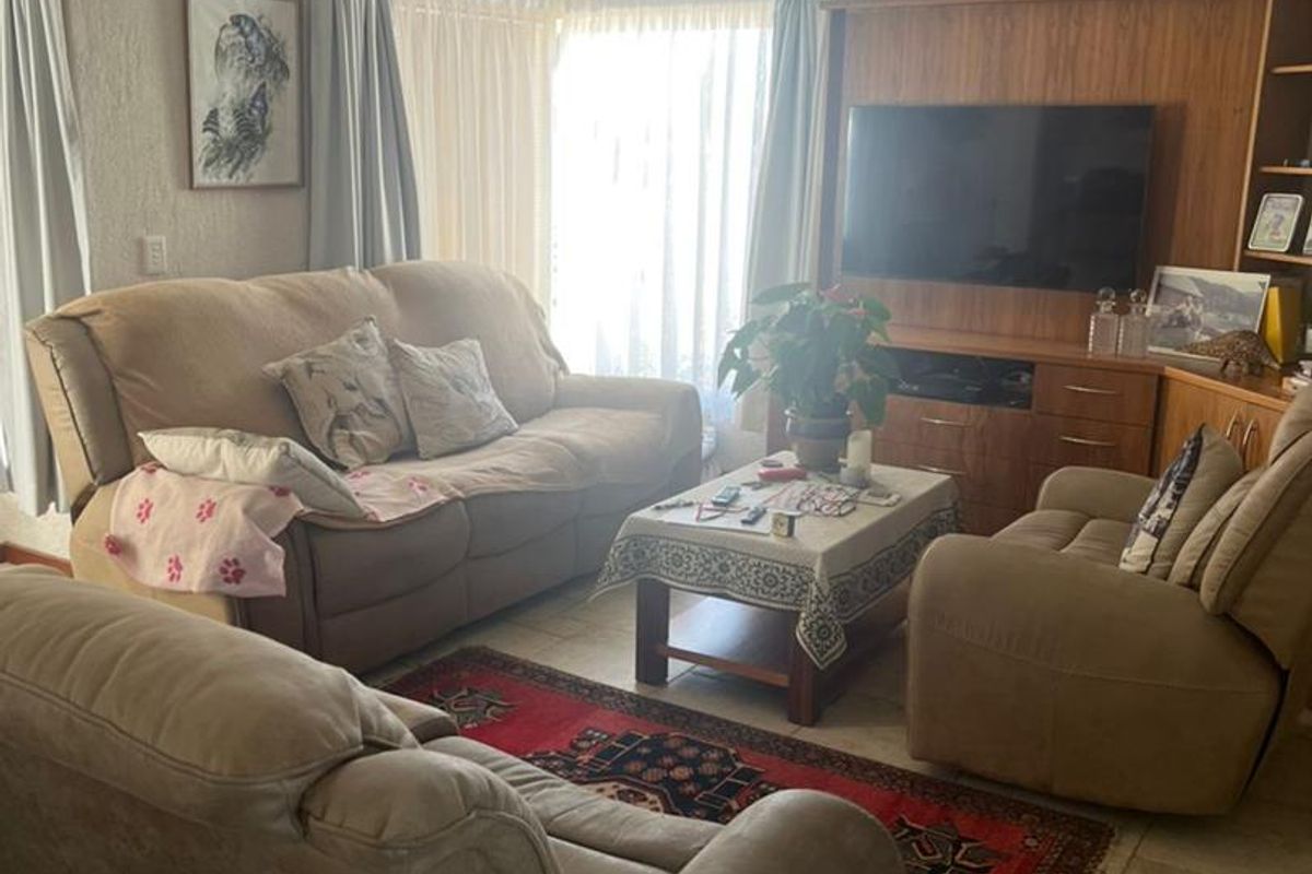 A comfortable living room featuring tiled flooring and a built-in wooden media unit, with natural light entering through large sliding glass doors.