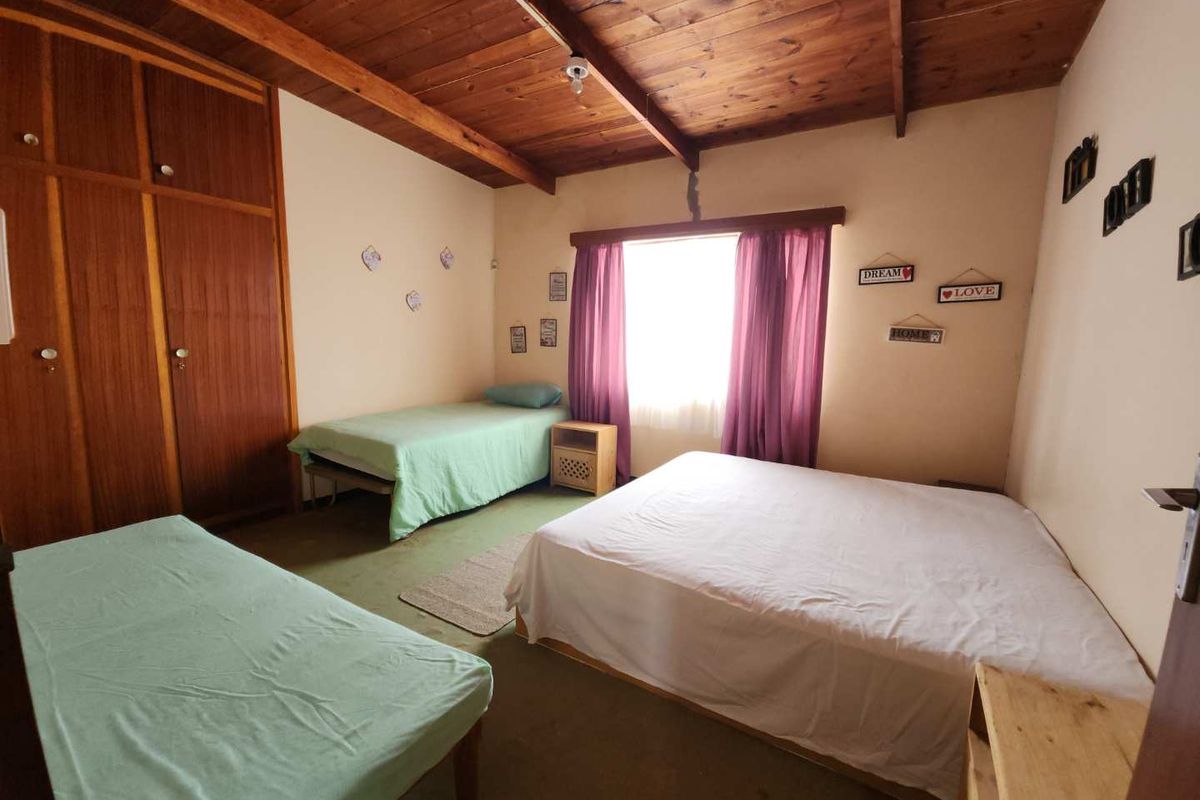 A bedroom featuring a timber-paneled ceiling, built-in wooden cupboards, and carpeted flooring, requiring some cosmetic updates.
