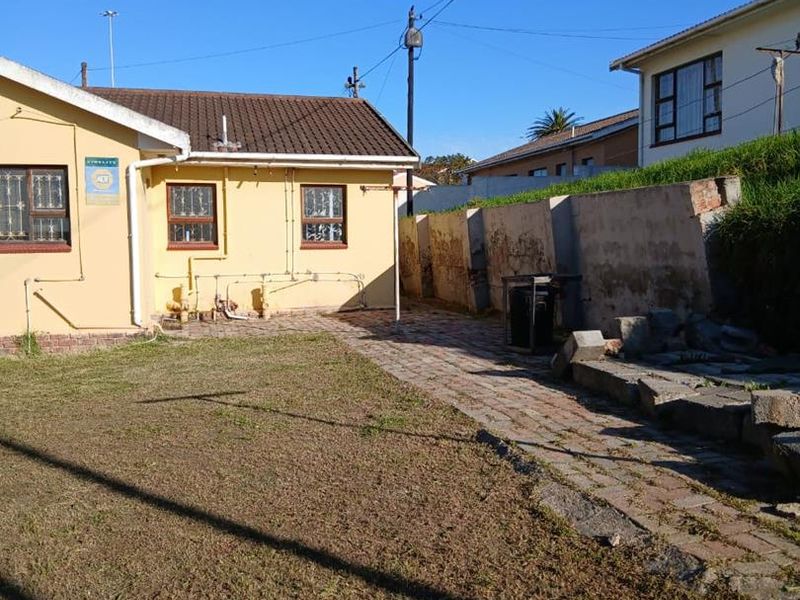 Rear exterior view of the property featuring a paved walkway, lawn area, and a retaining wall requiring maintenance.