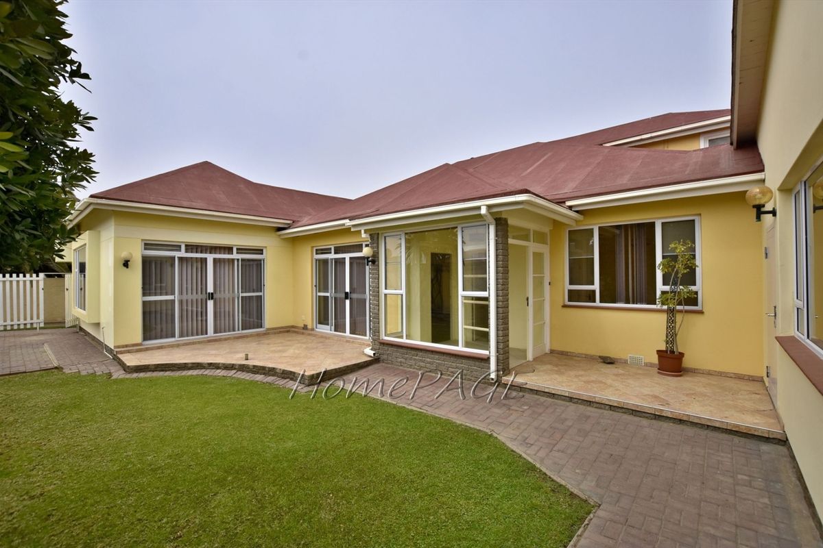 Rear view of the property featuring a paved patio area, landscaped garden, and multiple sliding glass doors providing access to the interior living spaces.