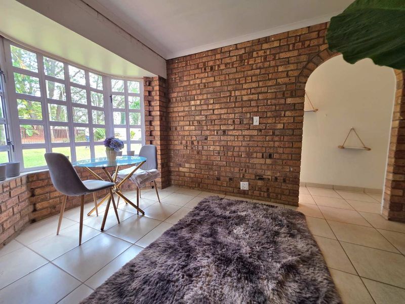 A bright living area featuring exposed brick walls, tiled flooring, and a large bay window that allows for ample natural light.