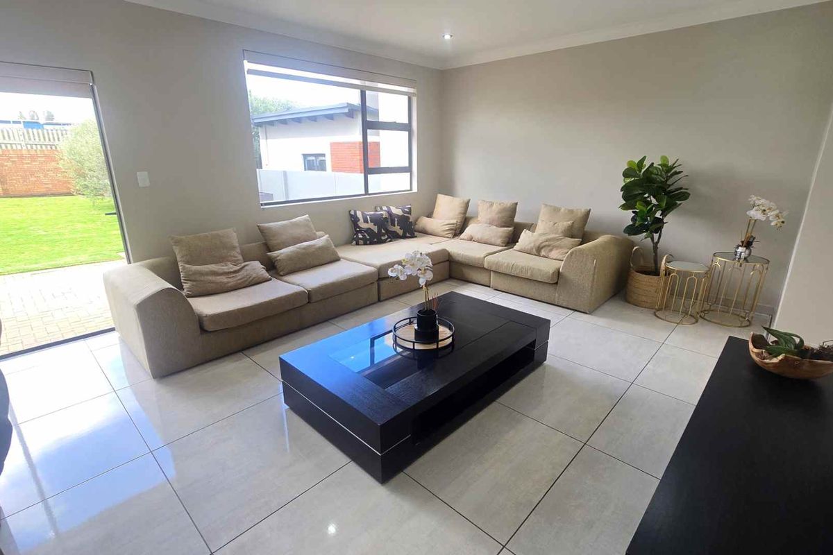 A bright and spacious living room featuring large format floor tiles, neutral wall tones, and a sliding door providing direct access to the garden.