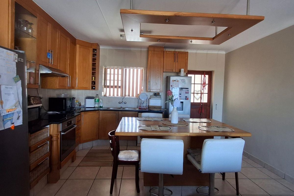 A functional kitchen featuring wooden cabinetry, built-in appliances, a central island with seating, and tiled flooring.