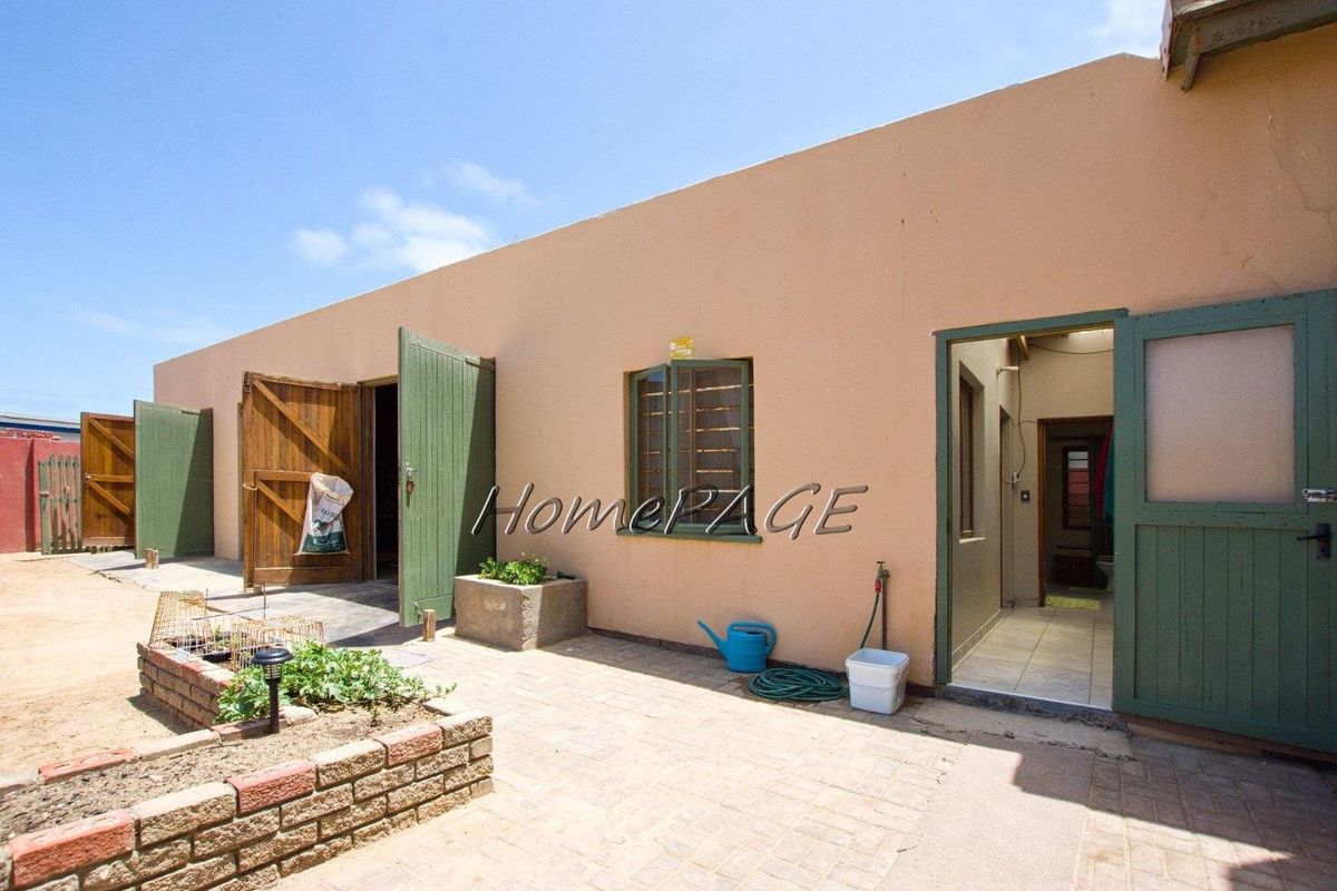 A rear exterior view of the property featuring paved courtyard area, brick planter boxes, and multiple access points with wooden doors.