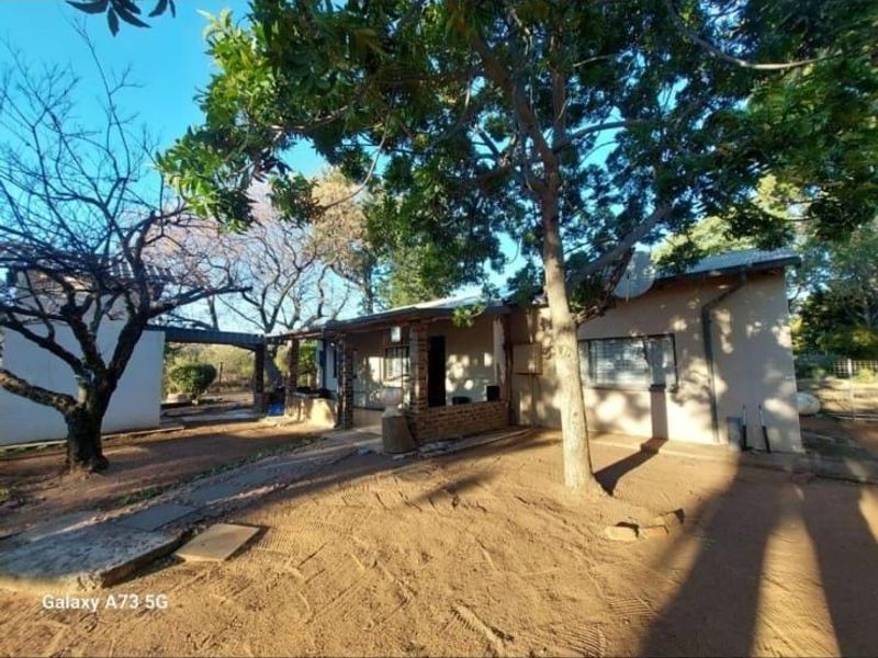 Rear view of the house featuring a covered patio area, brick masonry, and a large garden with mature trees.
