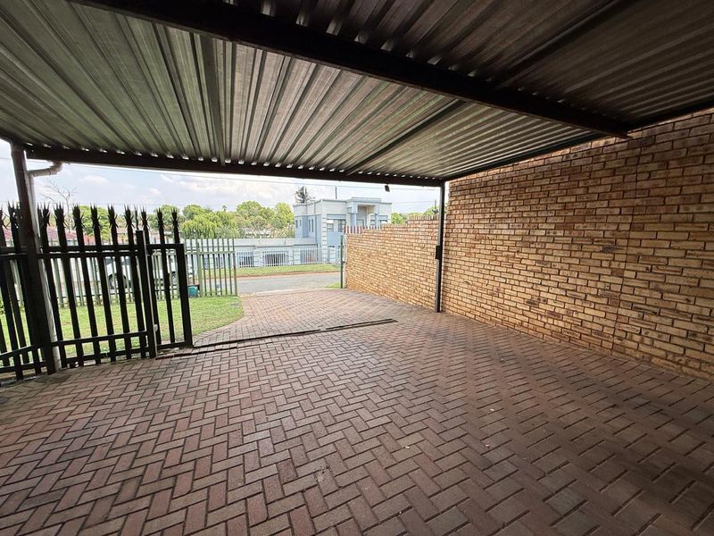 A covered carport area featuring a corrugated metal roof, brick walling, and paved flooring, secured by a metal gate.