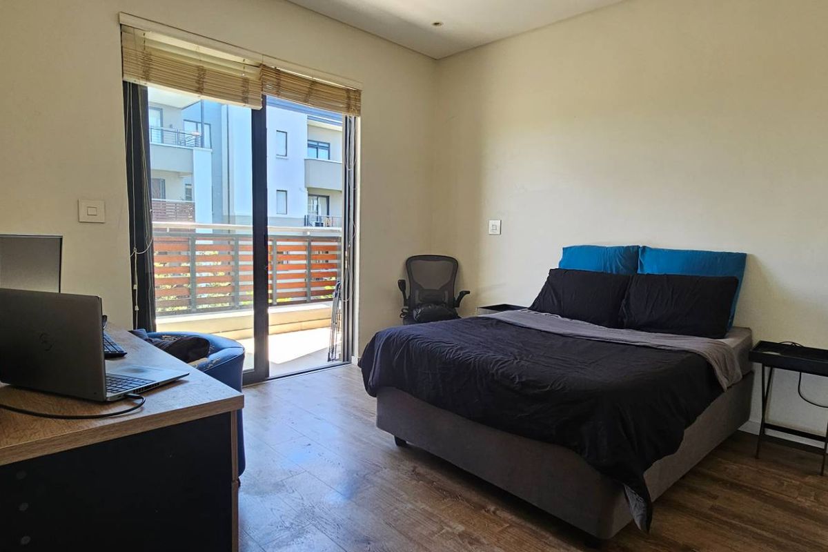 A well-lit bedroom featuring laminate flooring, neutral walls, and a sliding glass door providing direct access to a private balcony.