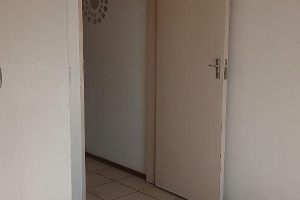 An empty bedroom featuring neutral tiled flooring and a built-in cupboard, offering a blank canvas for personalization.