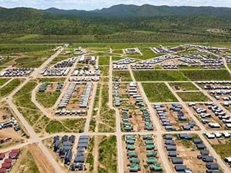 An aerial view of a large residential development featuring a grid of paved roads and numerous housing units set within a rural landscape.