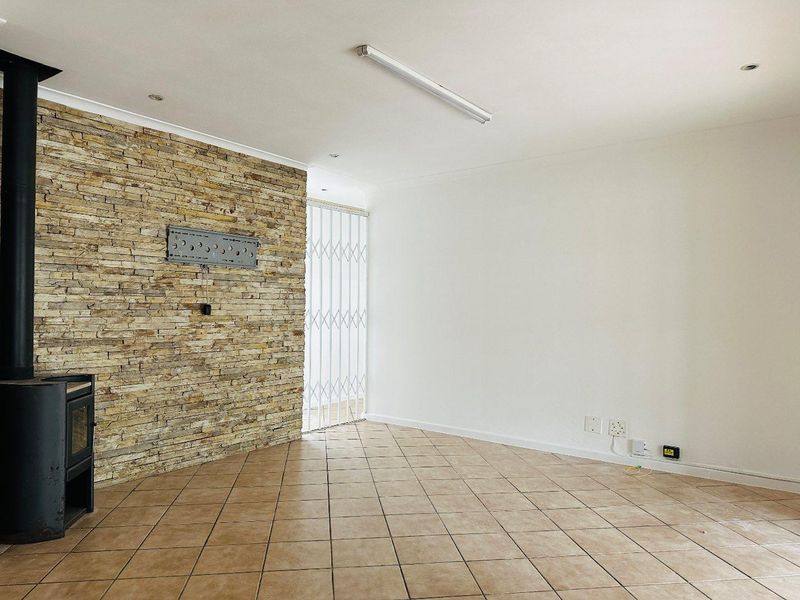 An empty living room featuring a stone accent wall, a freestanding fireplace, tiled flooring, and a security gate leading to the exterior.