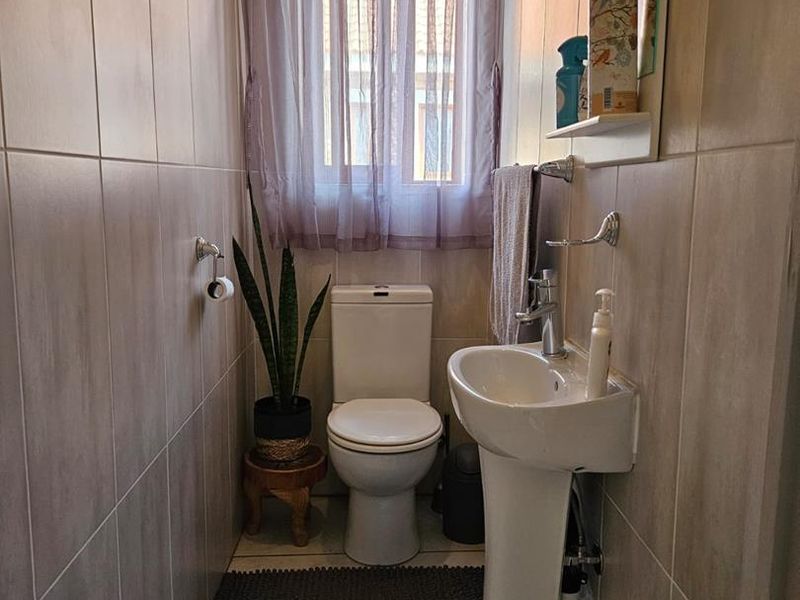 A compact guest bathroom featuring floor-to-ceiling tiling, a pedestal basin, and a standard toilet, providing a clean and functional space.