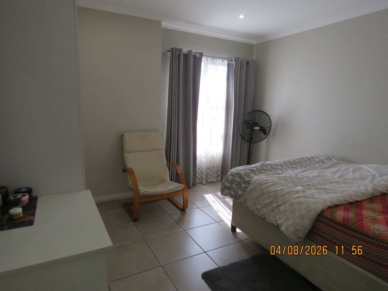 A functional bedroom featuring neutral wall tones, tiled flooring, and a built-in cupboard, offering a clean and simple living space.