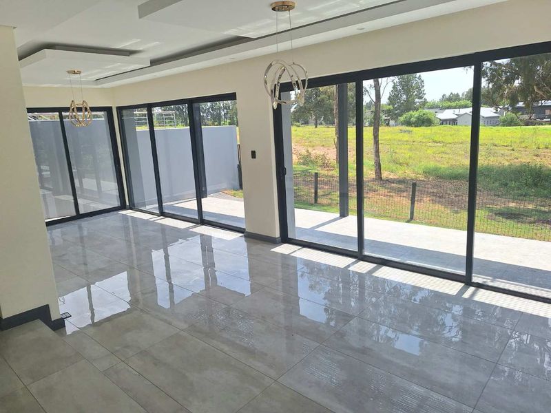 Spacious open-plan living area featuring large sliding glass doors, polished porcelain tile flooring, and modern recessed ceiling lighting with views of the garden.