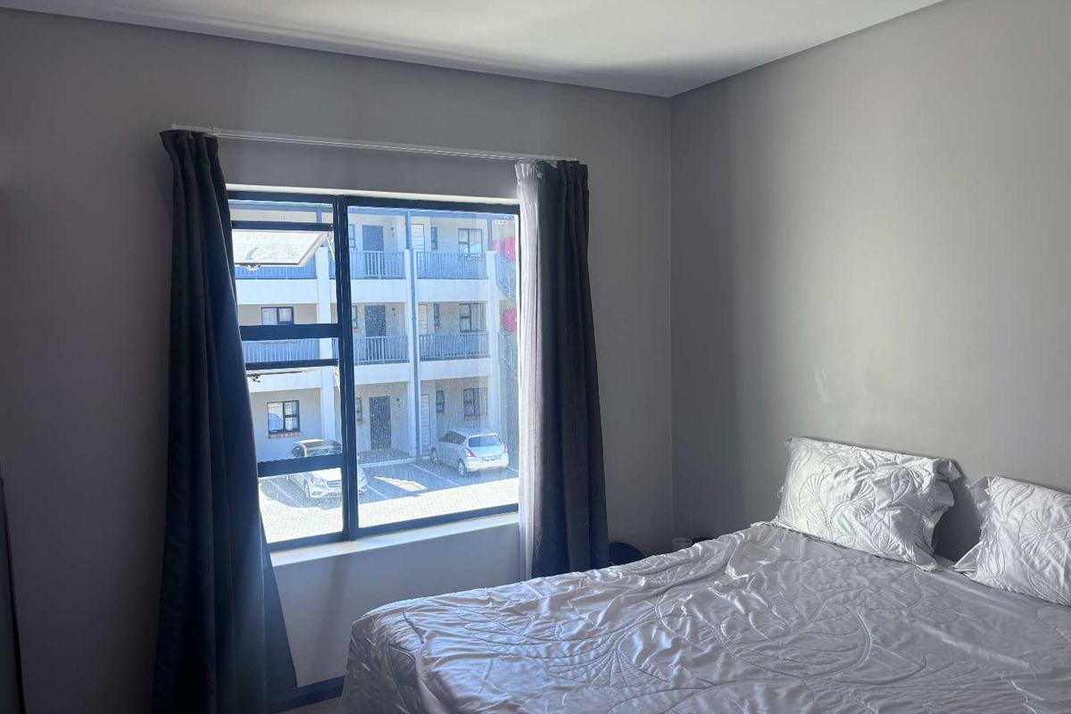 A well-lit bedroom featuring neutral grey walls, a large aluminium-framed window, and recessed ceiling lighting, offering a clean and modern living space.