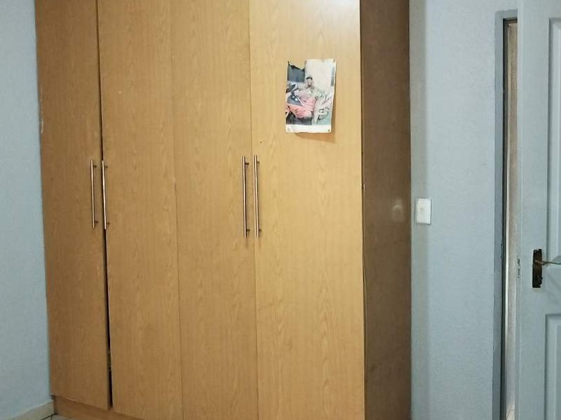 A bedroom featuring a large, light wood-finish built-in wardrobe and neutral tiled flooring.