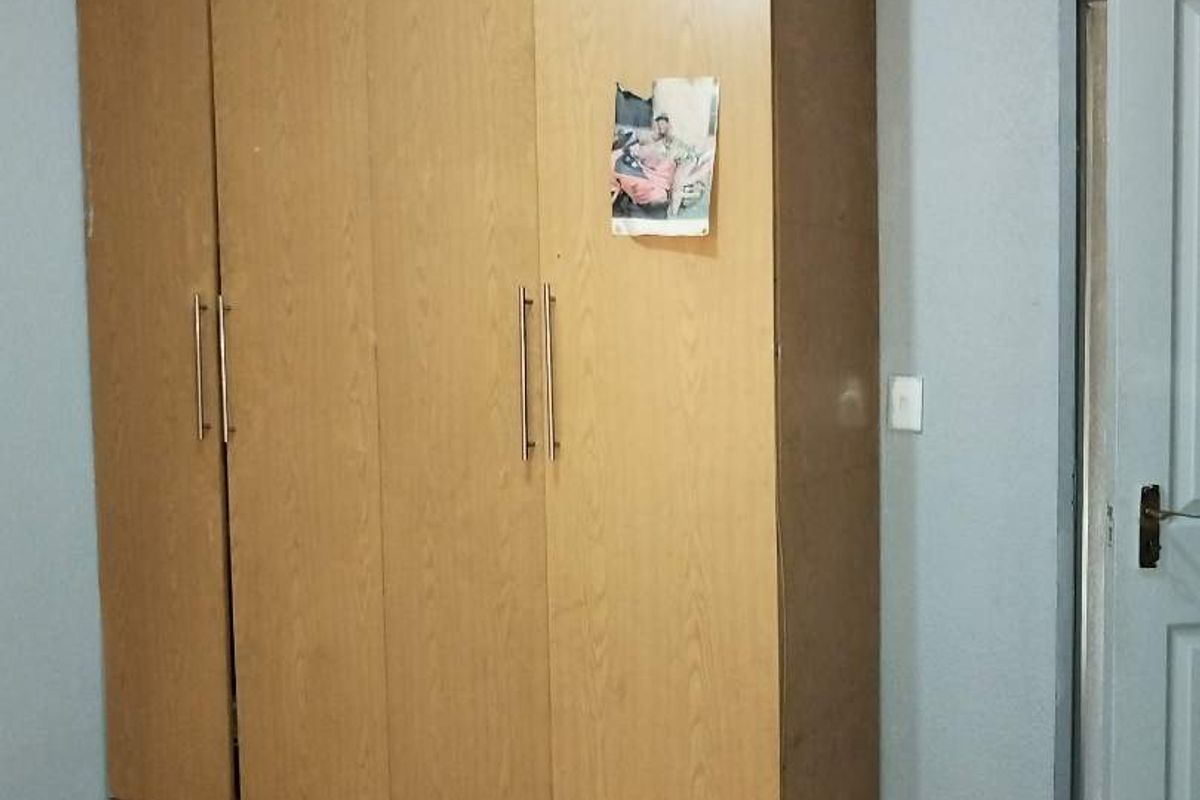 A bedroom featuring a large, light wood-finish built-in wardrobe and neutral tiled flooring.