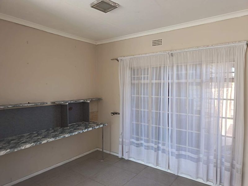 A vacant bedroom featuring tiled flooring, a built-in desk unit, and sliding glass doors providing access to the exterior.