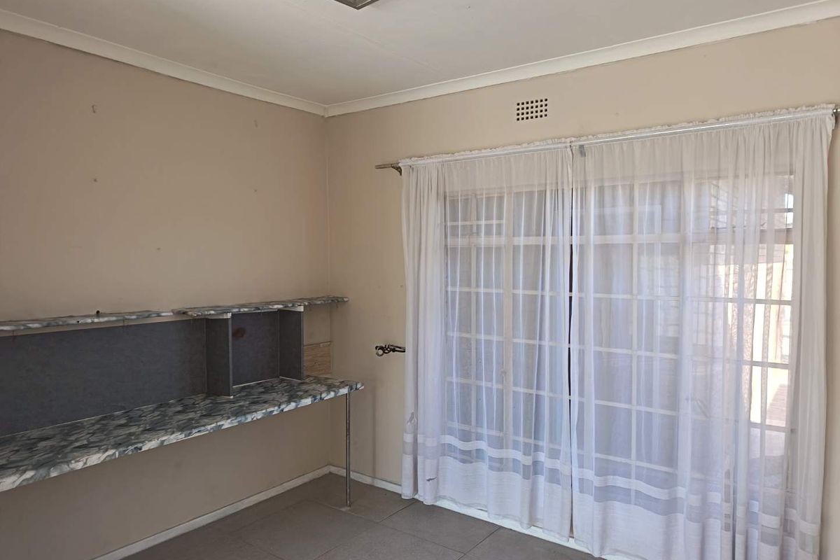 A vacant bedroom featuring tiled flooring, a built-in desk unit, and sliding glass doors providing access to the exterior.