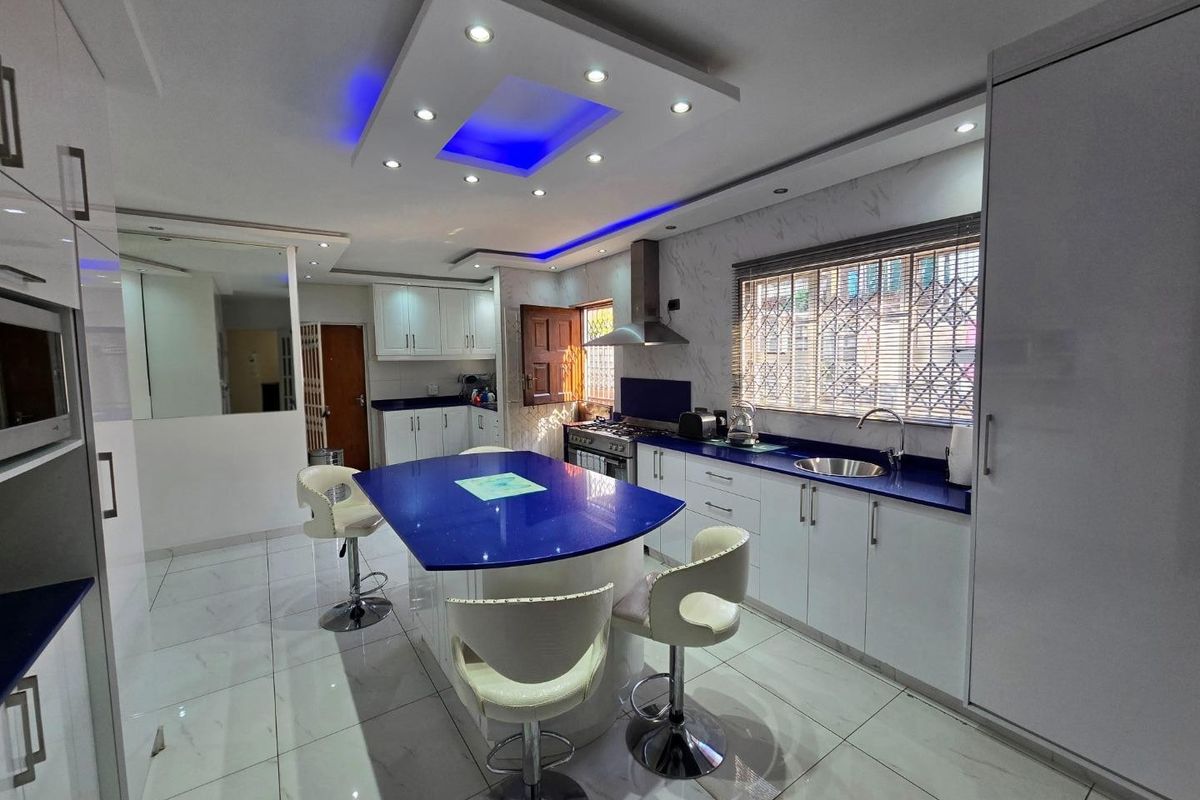 Modern kitchen featuring a central island with a blue countertop, white cabinetry, recessed ceiling lighting, and tiled flooring.