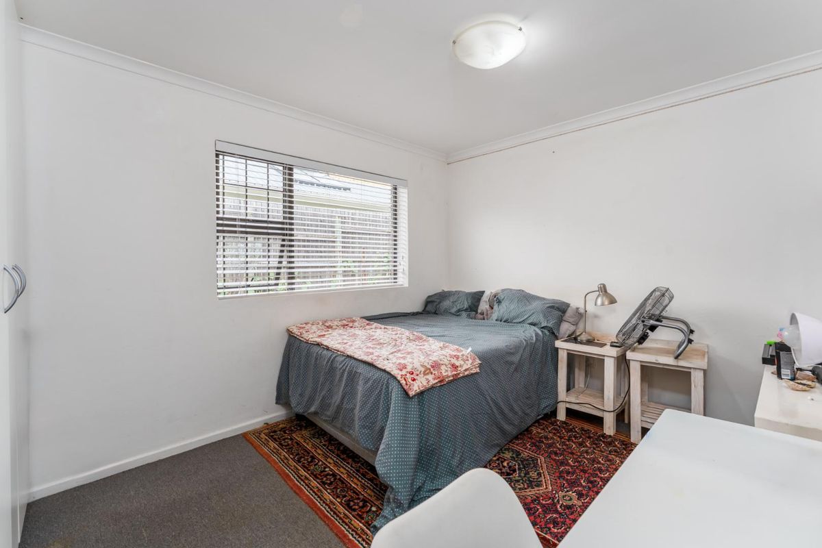 A functional bedroom featuring neutral walls, carpeted flooring, and a window with fitted blinds.