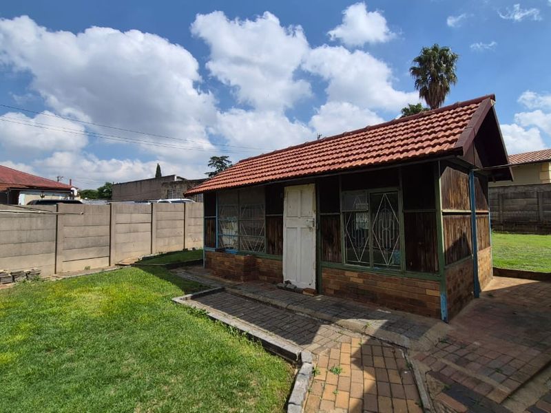 A detached outbuilding featuring a terracotta tiled roof, brick base, and timber cladding, situated in a backyard with a paved walkway and boundary wall.
