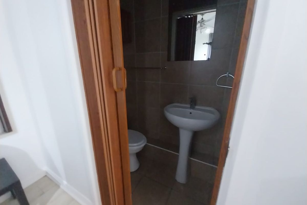 A compact bathroom featuring a pedestal basin, toilet, and dark tiled finishes, accessed via a wooden folding door.