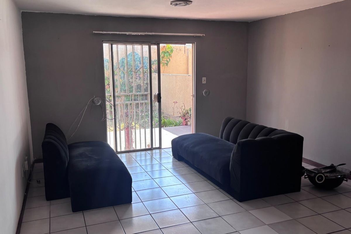 A living room featuring tiled flooring and a sliding glass door with a security gate, providing direct access to the outdoor area.