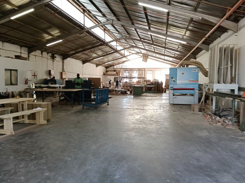 Spacious industrial workshop featuring high ceilings with exposed steel trusses, skylights, concrete flooring, and integrated dust extraction infrastructure.