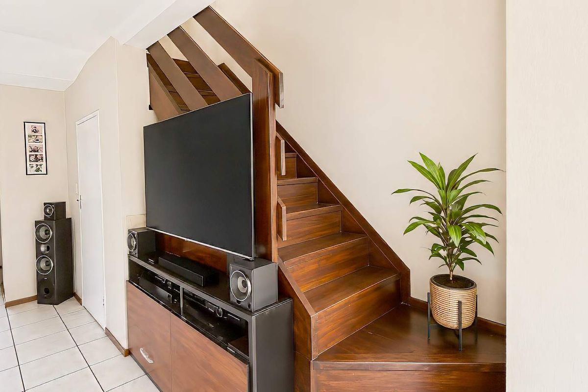 A living area featuring a wooden staircase with integrated storage and tiled flooring, leading towards an entrance hallway.