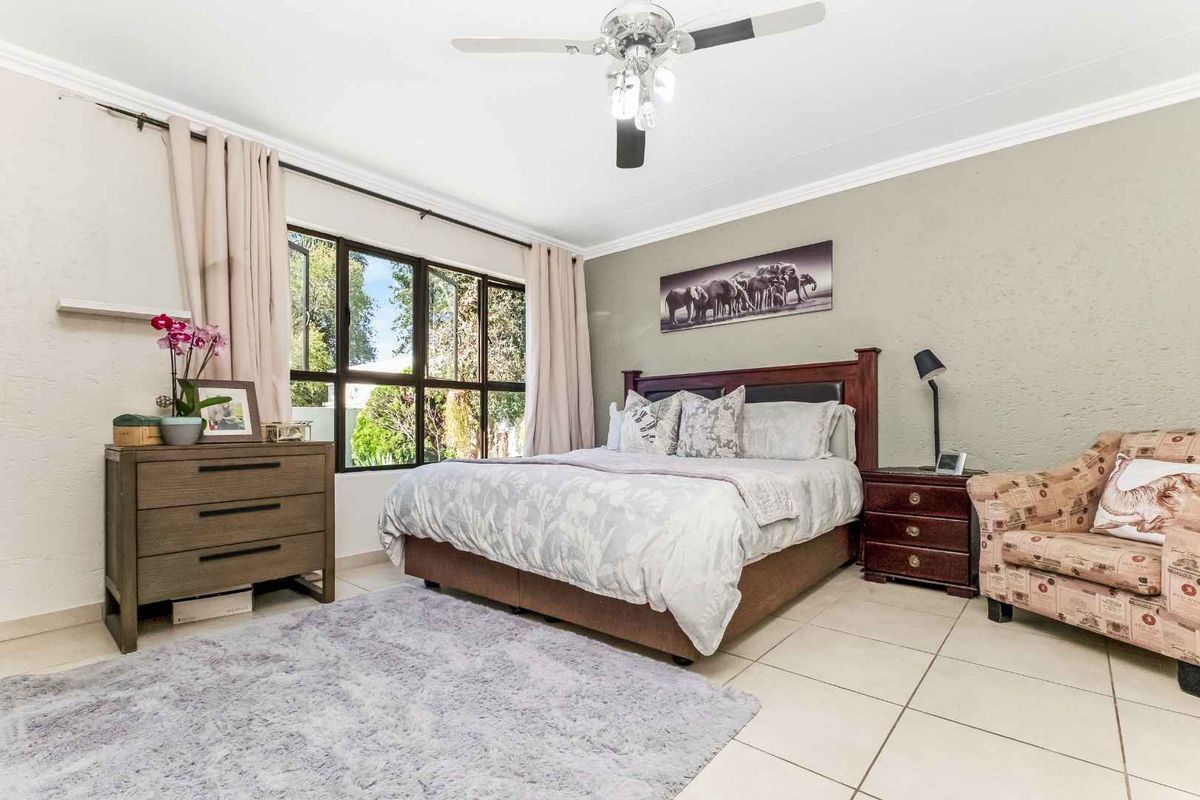 A well-lit bedroom featuring tiled flooring, a ceiling fan, and large windows that provide natural light and garden views.