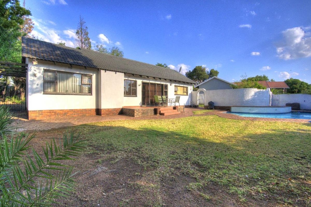Rear view of the property featuring a paved patio area, swimming pool, and a spacious garden with established landscaping.
