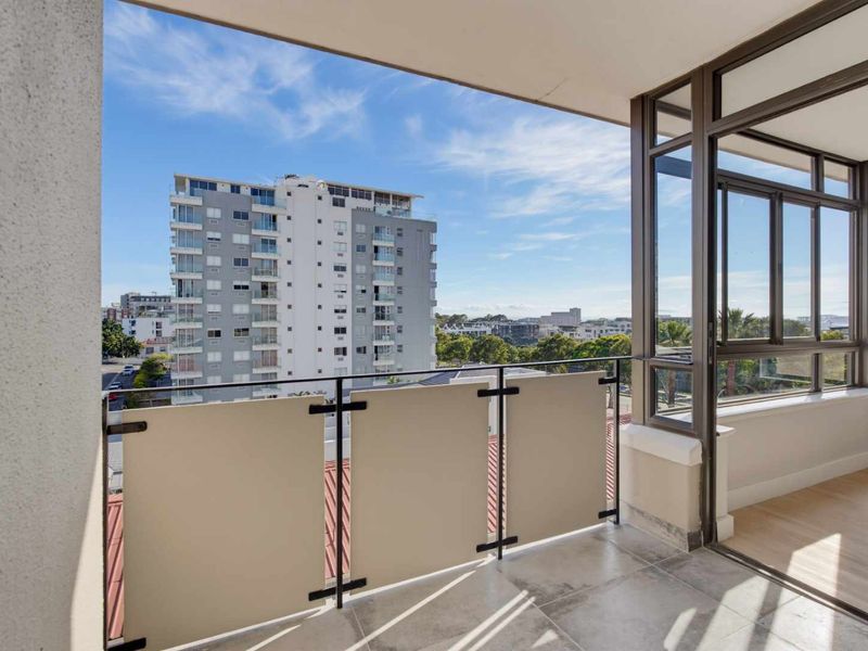 A clean, modern balcony featuring tiled flooring, a metal balustrade with privacy screens, and large sliding glass doors offering an urban city view.