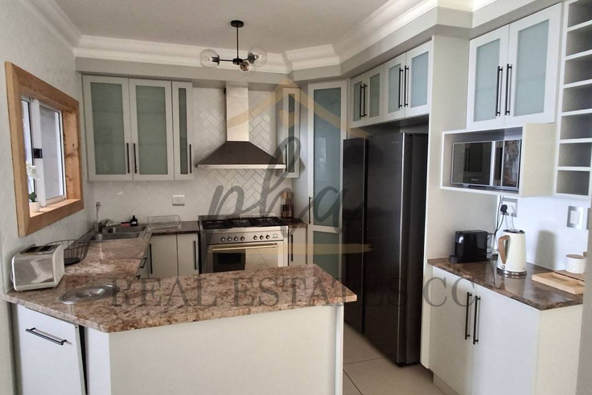 Modern kitchen featuring stone countertops, ample built-in cabinetry, a gas stove with extractor fan, and integrated microwave, finished with neutral tiled flooring.