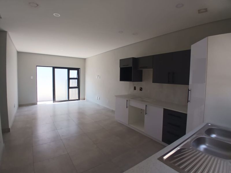 Modern open-plan living area featuring a contemporary kitchen with two-tone cabinetry, tiled flooring, and direct access to an outdoor space through sliding doors.