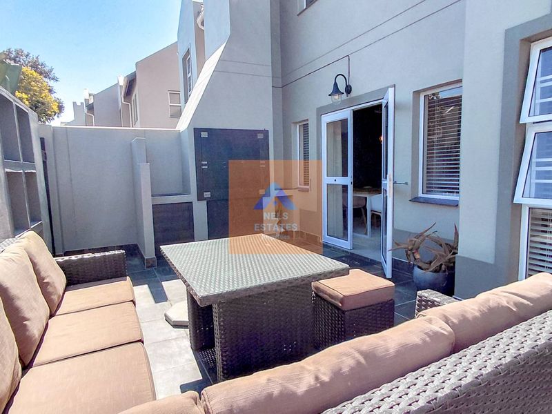 A paved outdoor patio area featuring a built-in braai, accessible via double glass doors from the main living space.