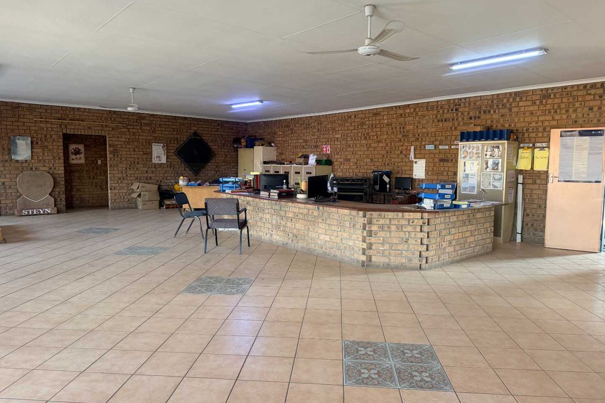 Spacious industrial office area featuring a built-in brick reception counter, tiled flooring, and exposed brick walls, suitable for a professional workspace.