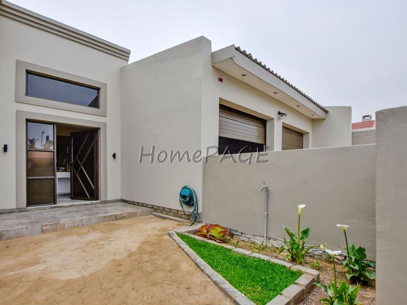 Rear exterior view of the property featuring a tiled patio area, landscaped garden bed, and secure roller shutters on the windows.