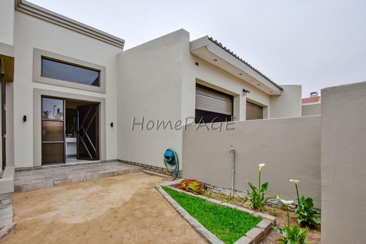 Rear exterior view of the property featuring a tiled patio area, landscaped garden bed, and secure roller shutters on the windows.